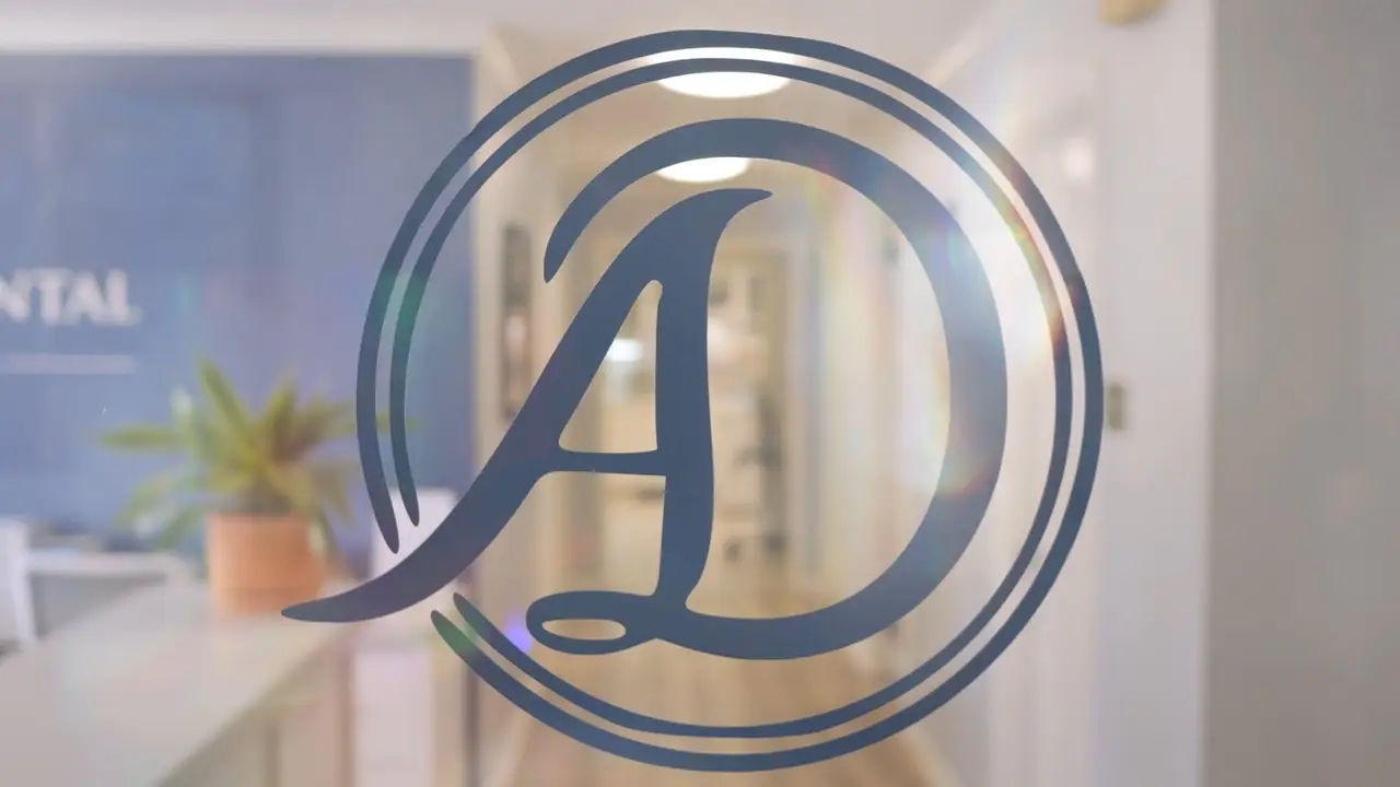 The Athens Dental Associates AD monogram on a glass door, with the reception desk and a corridor softly out of focus behind it.
