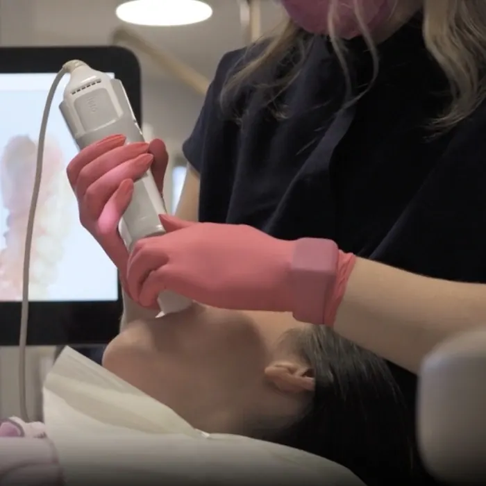 A team member in navy scrubs taking a digital impression of a patient's teeth with a handheld intraoral scanner.